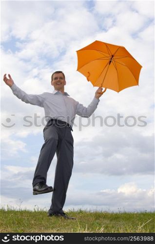 Happy laughing businessman with orange umbrella in a meadow