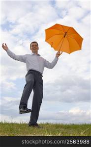Happy laughing businessman with orange umbrella in a meadow