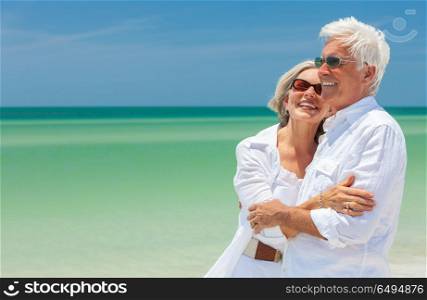 Happy laughing senior man and woman retired couple embracing wearing sunglasses on a deserted tropical beach with turquoise sea and clear blue sky. Happy Senior Couple Laughing Embracing on a Tropical Beach