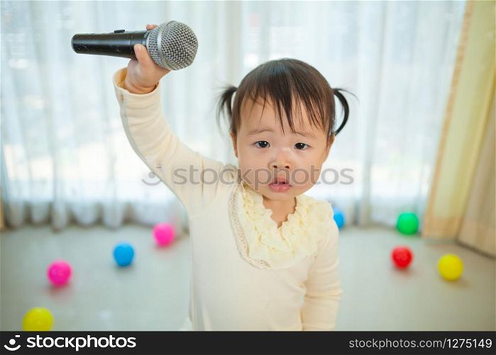 Happy little asian girl with microphone in the home