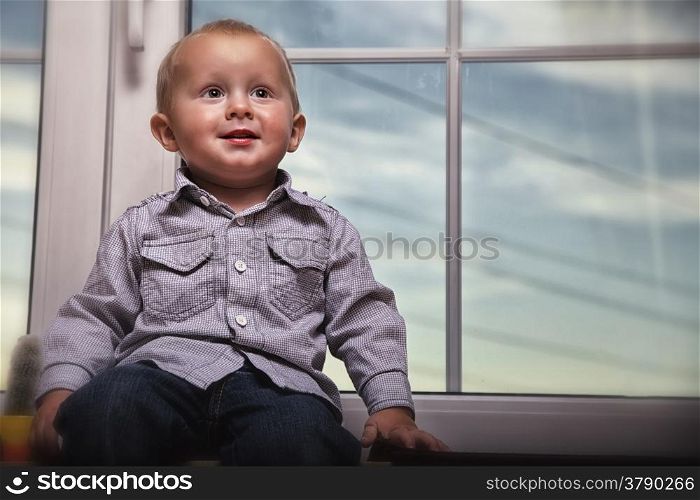 happy little boy blond sitting on window indoor