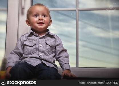 happy little boy blond sitting on window indoor