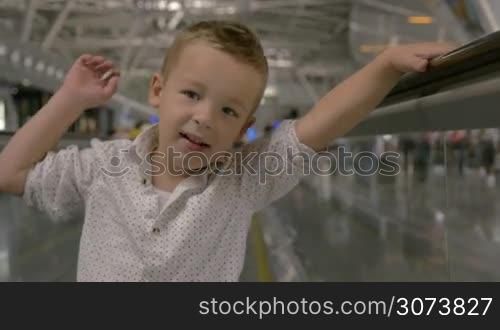 Happy little boy riding on flat escalator in trade centre. Funny child waving hand in greeting and giving kiss