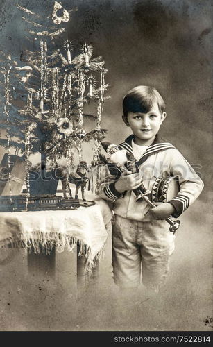 Happy little boy with christmas tree, gifts and vintage toys. Antique sepia picture with original film grain and scratches