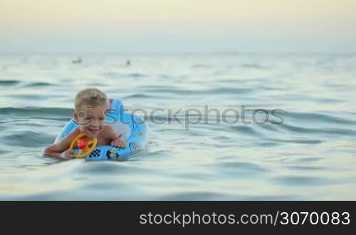 Happy little boy with rubber ring made as car swimming in sea. Summer vacation