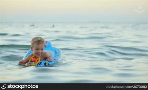 Happy little boy with rubber ring made as car swimming in sea. Summer vacation