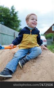 Happy little boy with toy shovel sitting on sand hill