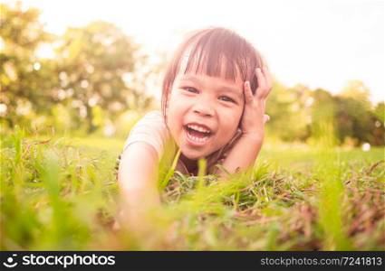 Happy little child girl lying on green grass outdoors in summer park.