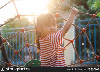 Happy little girl climbing on rope mesh at playground. An active little girl in the outdoor playground. Healthy summer activity for children.