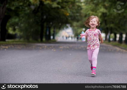 happy little girl drinking fresh water from a bottle while running at city park