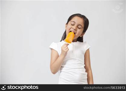 Happy little girl eating ice lolly isolated over gray background