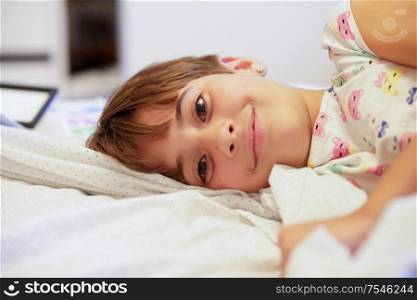 Happy little girl, eight years old, lying on her bed at home. smiling to camera.. Little girl, eight years old, lying on her bed