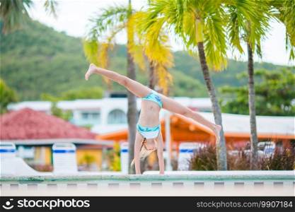Happy little girl enjoy vacation in the swimming pool. Sporty kid making cartwheel on the edge of pool. Happy little girl enjoy vacation in the swimming pool.