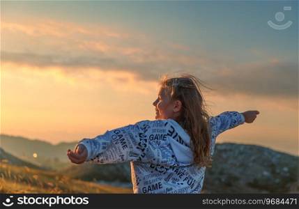 Happy little girl having fun in the mountains. Happy child with raised up hands enjoying mild sunset light. Summer c&in the mountains.. Cheerful little girl the mountains