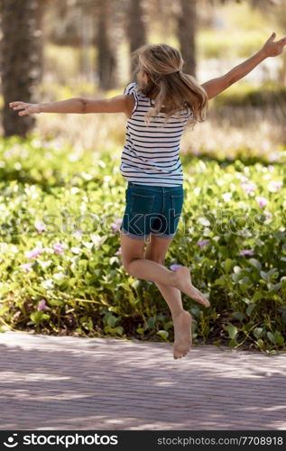 Happy Little Girl Having Fun in the Park. Cheerful Child Playing Games and Jumping on the Way. Carefree Childhood. Enjoying Summer Holidays.. Little Girl in the Park