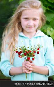 Happy little girl holding a bush of wild strawberries