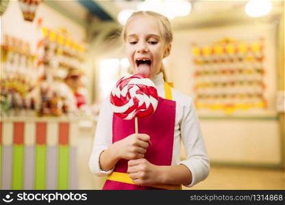 Happy little girl holds fresh lollipop in candy store. Handmade sugar caramel on stick. Happy little girl holds fresh lollipop