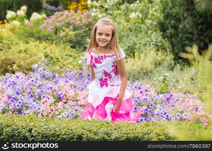 Happy little girl in a long dress at flower bed. Happy six year old girl in a lush evening pink dress walking through the green garden