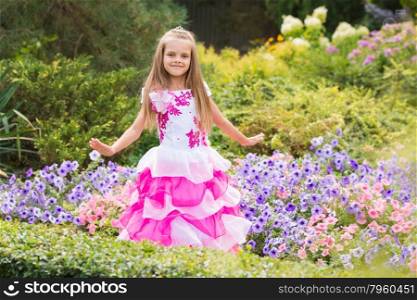 Happy little girl in a pink dress at flower bed. Happy six year old girl in a lush evening pink dress walking through the green garden