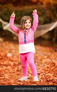 Happy little girl in autumn park, enjoying beautiful fall nature, raised up hands and playing with dry tree leaves, happy carefree childhood