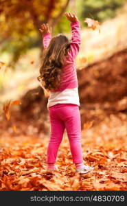 Happy little girl in autumn park, rear view of a nice child throwing up dry tree leaves, playing outdoors in a warm fall day, happy carefree childhood