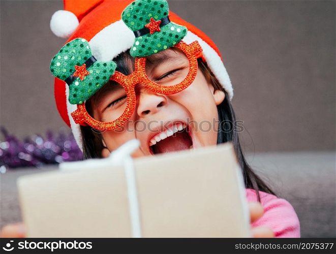 Happy little girl in Santa hat giving a Christmas present at home. Happy New Year and Merry Christmas.