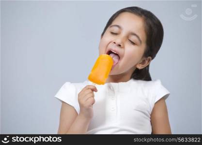 Happy little girl licking ice lolly isolated over gray background