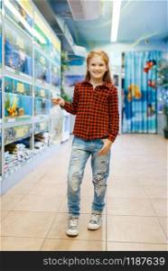 Happy little girl looking on goldfish in pet store. Child buying equipment in petshop. Happy little girl looking on goldfish in pet store