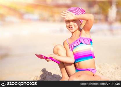 Happy little girl playing on the beach with shovel and sandbag in bright sunny day, active childhood, having fun outdoors, enjoying summer holidays on the seashore