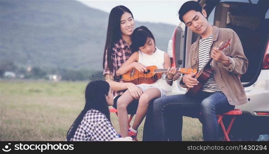 happy little girl playing ukulele with asian family sitting in the car for enjoying road trip and summer vacation,soft focus
