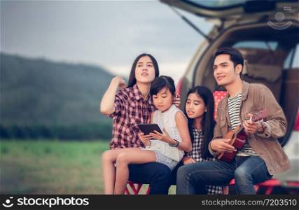 happy little girl playing ukulele with asian family sitting in the car for enjoying road trip and summer vacation