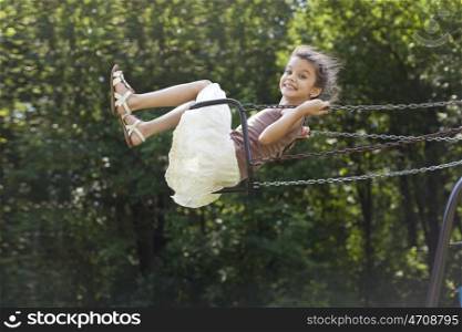 Happy little girl riding on a swing in the park