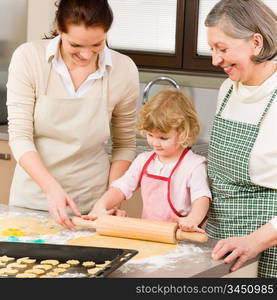 Happy little girl rolling out dough with mum and grandmother