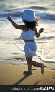 Happy little girl running on the sand along the sea on the beach