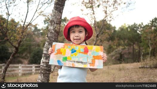 Happy little girl showing her coloring work in cardboard in the garden.