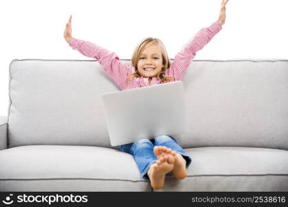 Happy little girl sitting on a couch and working a laptop