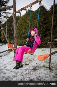 Happy little girl swinging on playground at snowy winter day