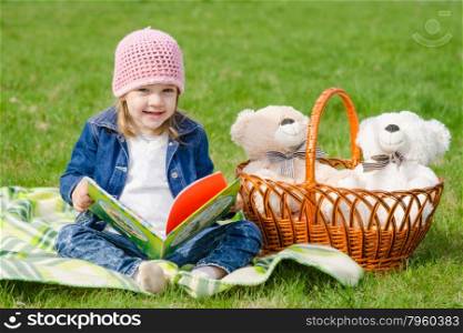 Happy little girl with a book on a picnic. The three-year girl is considering a book on picnic