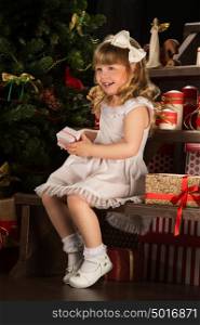 Happy little girl with Christmas gifts sitting near Christmas tree