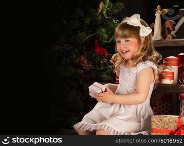 Happy little girl with Christmas gifts sitting near Christmas tree. Lots of copyspace