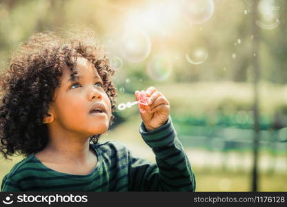 Happy little kid blowing soap bubble in school garden. Child outdoor activity concept.