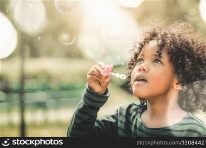 Happy little kid blowing soap bubble in school garden. Child outdoor activity concept.. Happy little kid blowing bubble in school garden.