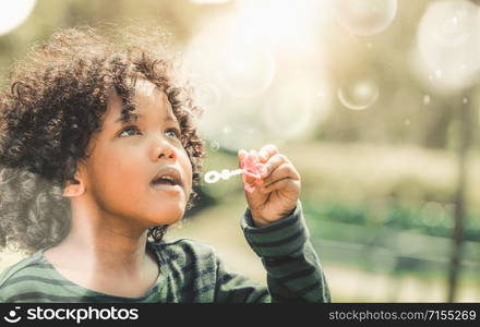 Happy little kid blowing soap bubble in school garden. Child outdoor activity concept.