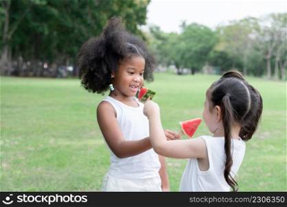 Happy little kids African and Caucasian picnic in the park. They eating sharing and feeding each other with watermelon on stick. Diverse ethnicity children friends enjoy life on summer