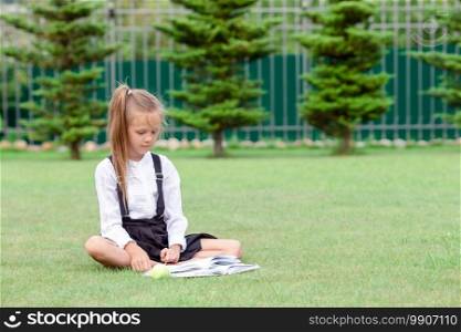 Happy little schoolgirl outdoors writing in her notebook. Happy little schoolgirl with a chalkboard outdoor