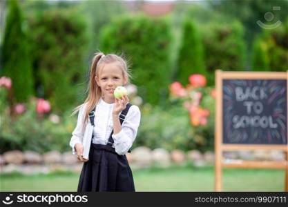 Happy little schoolgirl with an apple background the chalkboard. Back to school outdoors. Happy little schoolgirl with a chalkboard outdoor