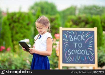 Happy little schoolgirl with laptop background on the chalkboard. Back to school outdoors. Happy little schoolgirl with a chalkboard outdoor
