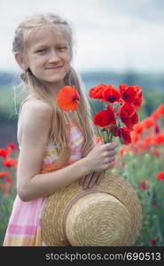 Happy little smiling girl in a hat at the amazing field of beautiful red poppy field in the countryside.