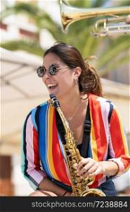 Happy looking young beautiful woman wearing glasses and holding a golden saxophone on an out of focus background. Street music and lifestyle concept.