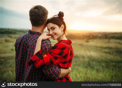 Happy love couple hugs in summer field at sunset. Romantic junket of man and woman, picnic on the meadow